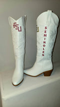 A pair of white faux leather cowboy boots featuring 'Seminoles' themed details, including vertical orange 'Seminoles' text on one boot and an orange and green 'U' logo on the other. Florida State Football Gameday